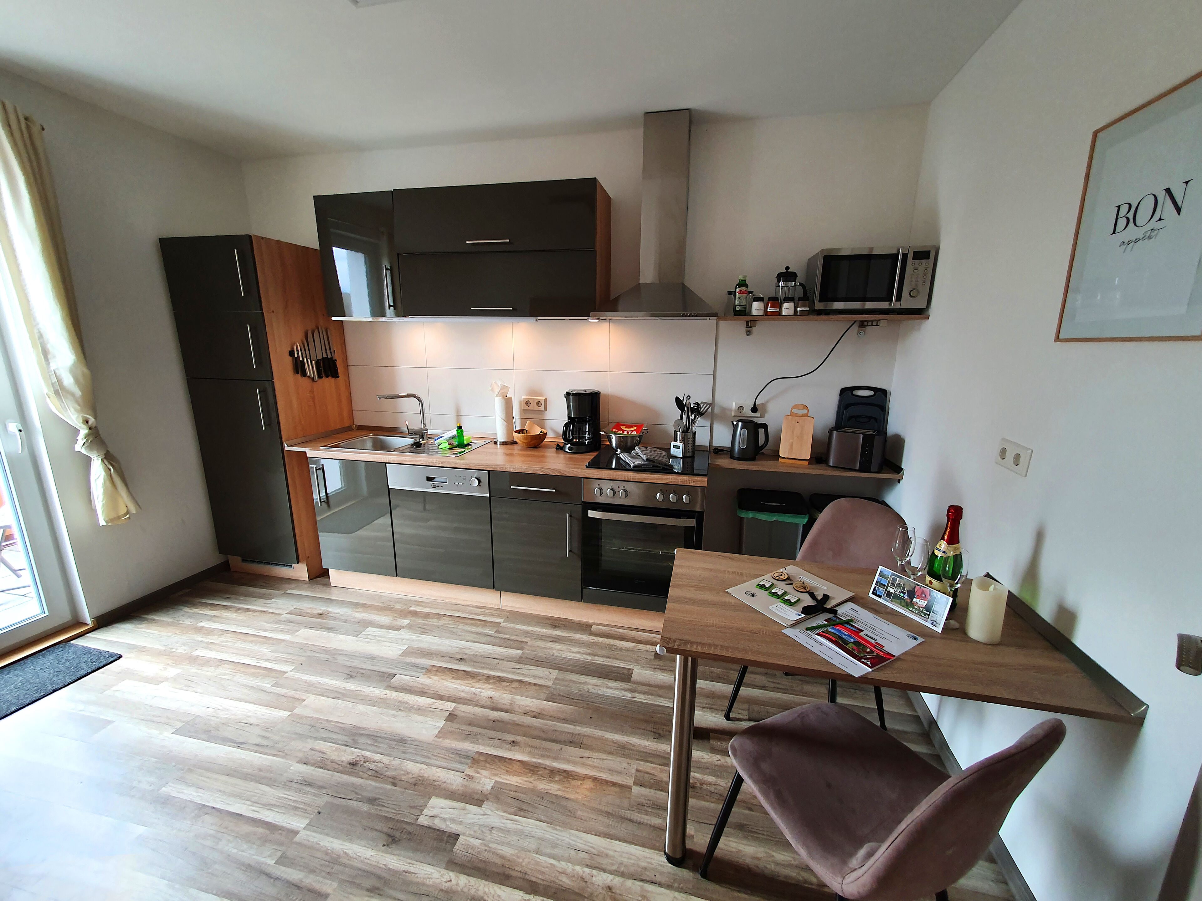 Een compacte keuken met moderne apparaten, een eethoek met een tafel en stoel, en een kleine prullenbak.