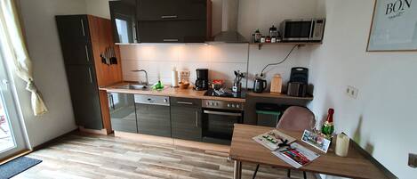 Een compacte keuken met moderne apparaten, een eethoek met een tafel en stoel, en een kleine prullenbak.