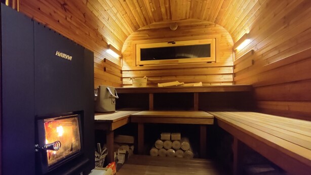 A sauna room with wooden walls and benches, a fireplace, and a Harvia sauna heater.