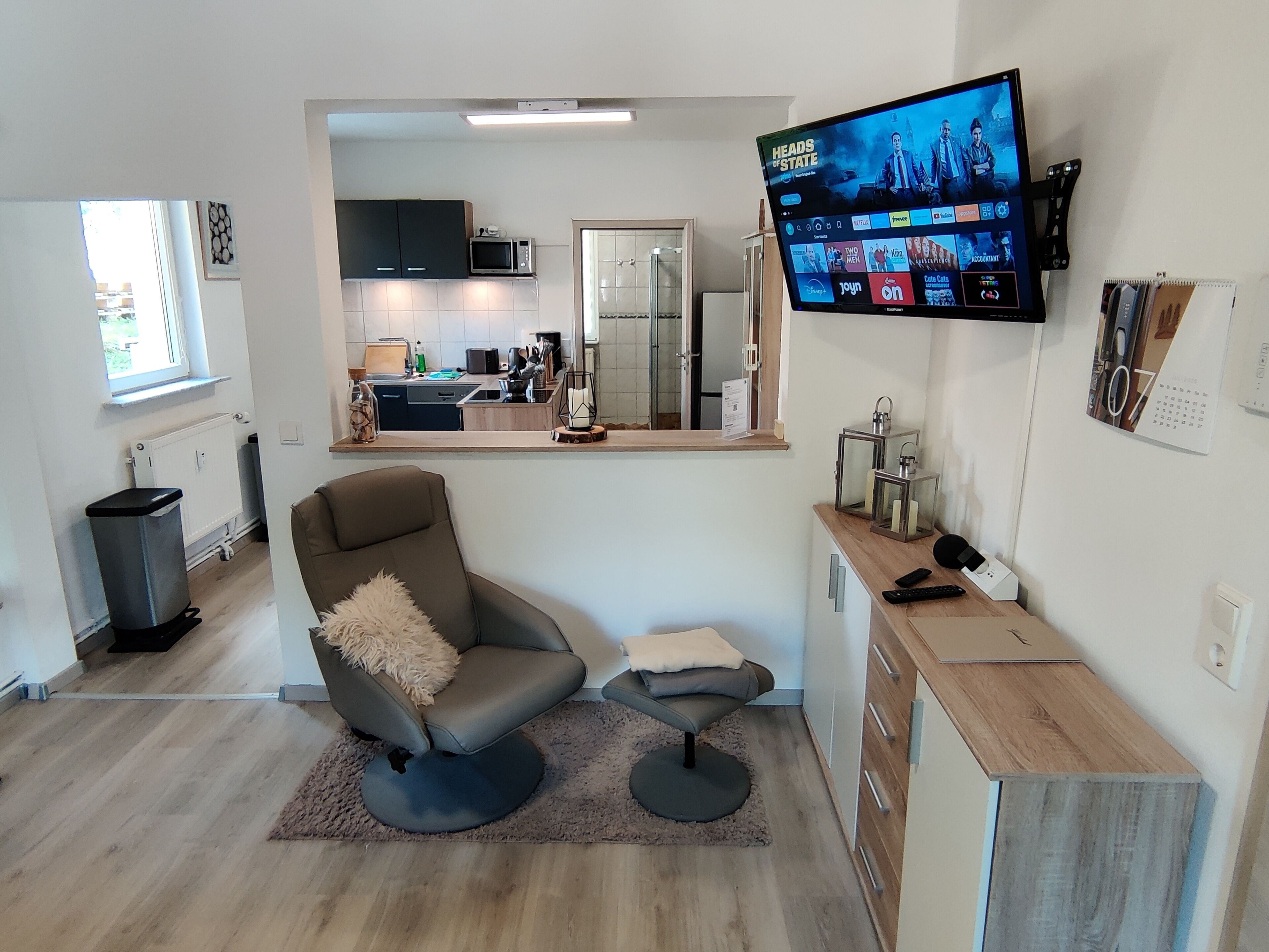 Een moderne woonkamer met een televisie, een bank, een salontafel en een keuken op de achtergrond.