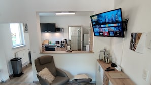 A modern living room with a TV, a sofa, a small table, and a kitchen in the background.