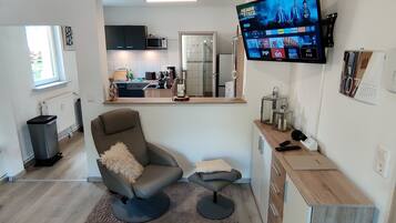 Een moderne woonkamer met een televisie, een bank, een salontafel en een keuken op de achtergrond.