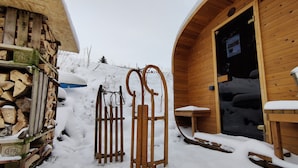 A wooden cabin with a snow-covered entrance, a stack of firewood, and a bench outside.