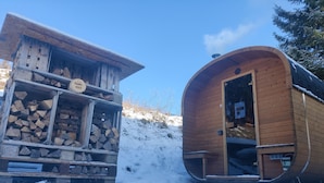 A wooden cabin with a sauna and a log storage area, surrounded by snow.