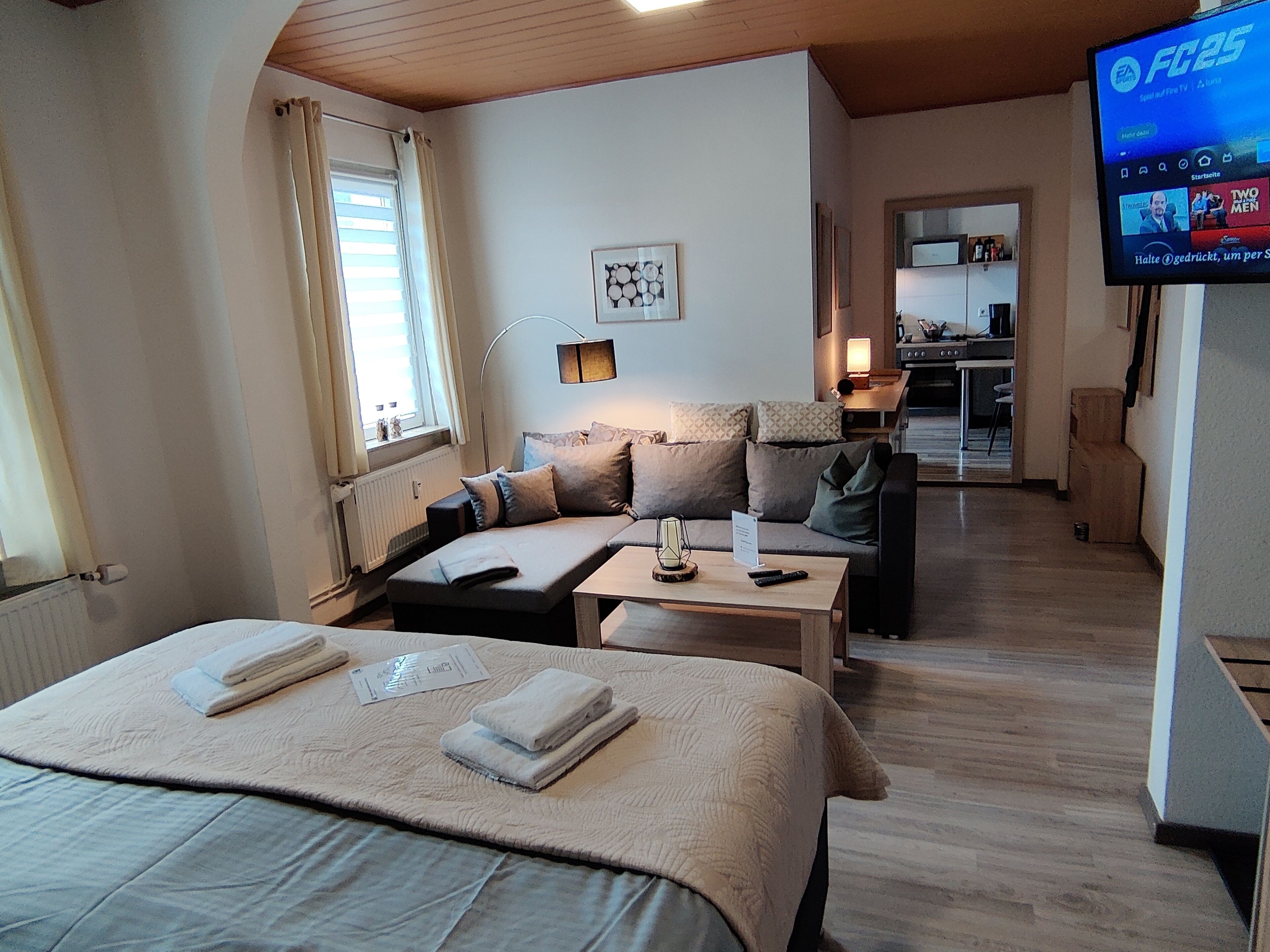 Een hotelkamer met een bed, een bank, een kleine tafel, een televisie en een keuken in de achtergrond.