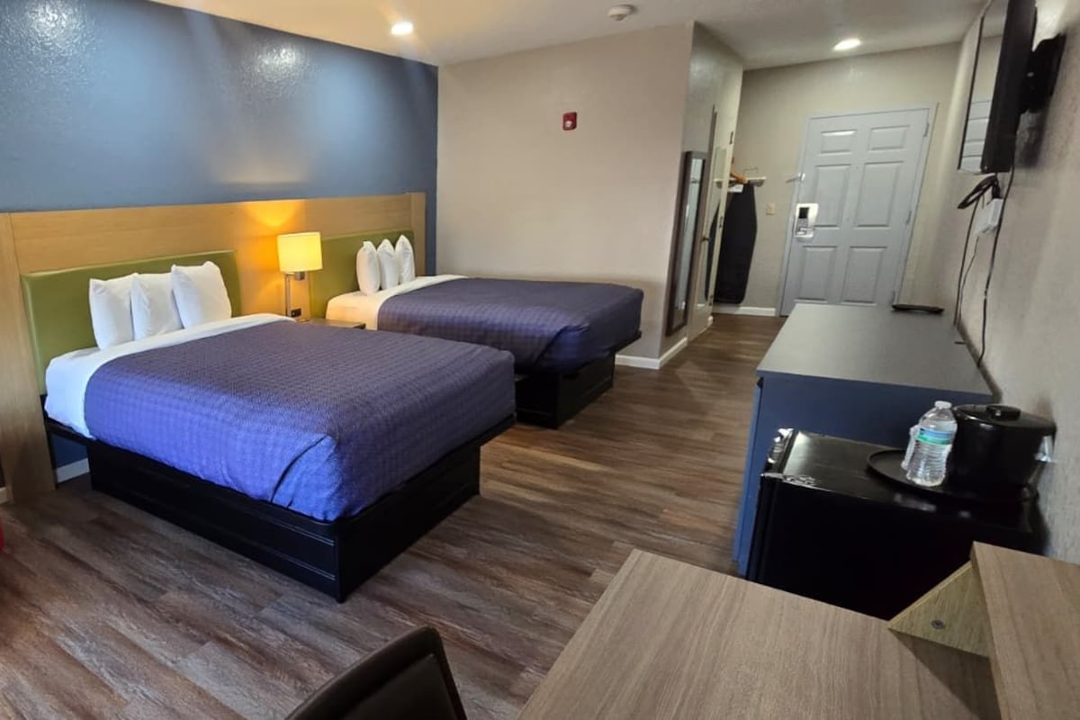 Une chambre d’hôtel avec deux lits, un fauteuil rouge, un bureau et une kitchenette.