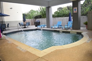 Une piscine avec des chaises longues bleues et un espace barbecue abrité.