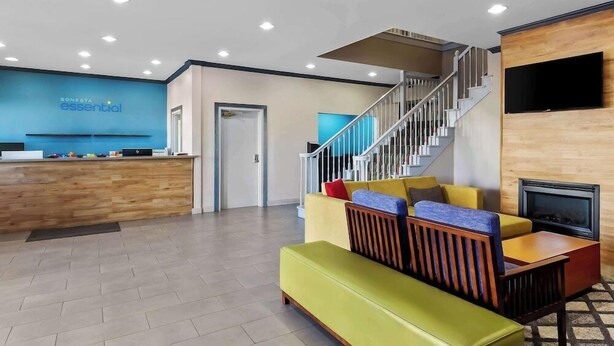 Un vestíbulo moderno con una recepción, una escalera, un área de descanso con cojines de colores y un televisor de pantalla plana montado en la pared.
