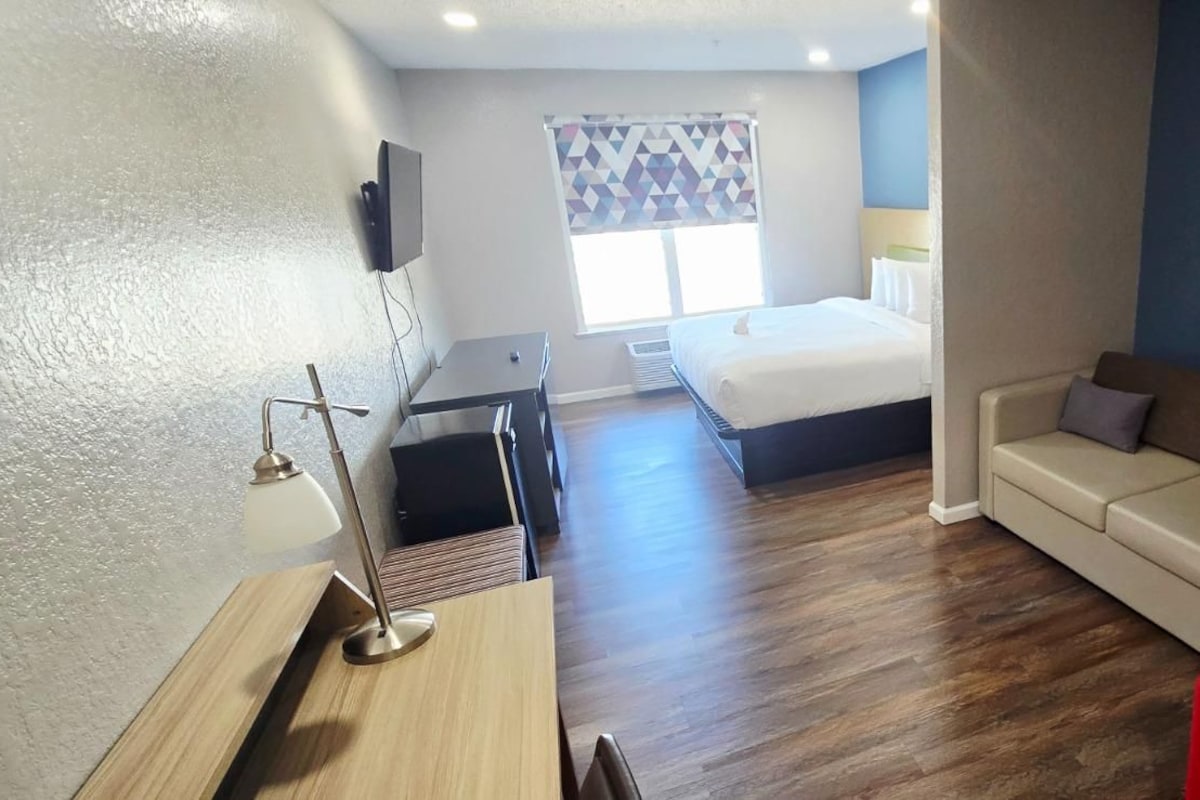 Une chambre d’hôtel avec un lit, un bureau, une chaise rouge, un canapé et un téléviseur.