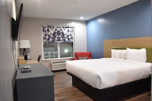 Une chambre d’hôtel équipée d’un lit, d’un bureau, d’une chaise, d’une télévision et d’une fenêtre avec des stores.
