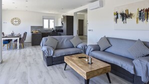 Una sala de estar moderna con un sofá gris, una mesa de centro de madera y un comedor con una mesa y sillas blancas.