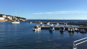 Una marina con varias embarcaciones amarradas, cielo azul despejado y una costa con edificios.