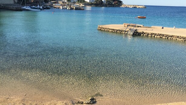 Un puerto deportivo con barcos amarrados, agua cristalina y una playa de arena con un muelle.