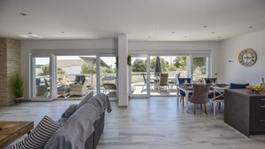 Amplia sala de estar con un sofá gris, una mesa de comedor con sillas y una zona de cocina.