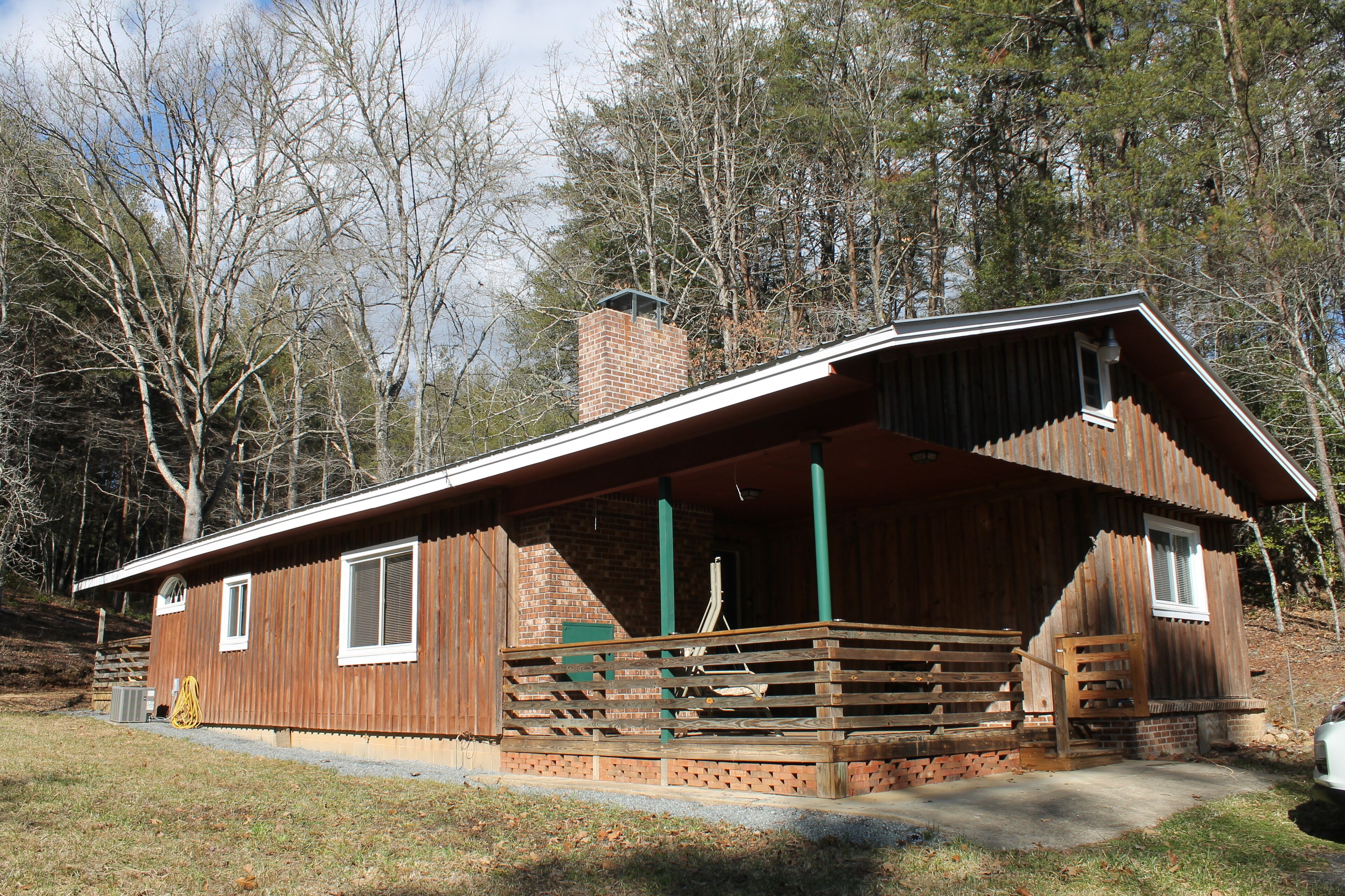 Une cabane rustique avec une façade en bois, une cheminée en briques et une véranda dotée d’une balustrade en bois.