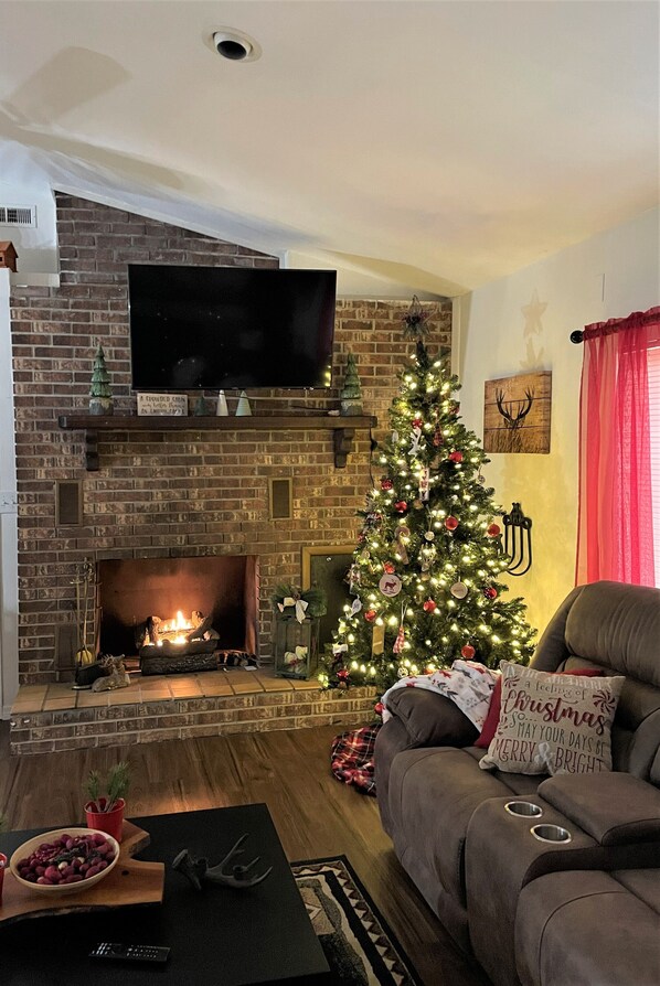 A cozy living room with a brick fireplace, a Christmas tree, and a comfortable couch.