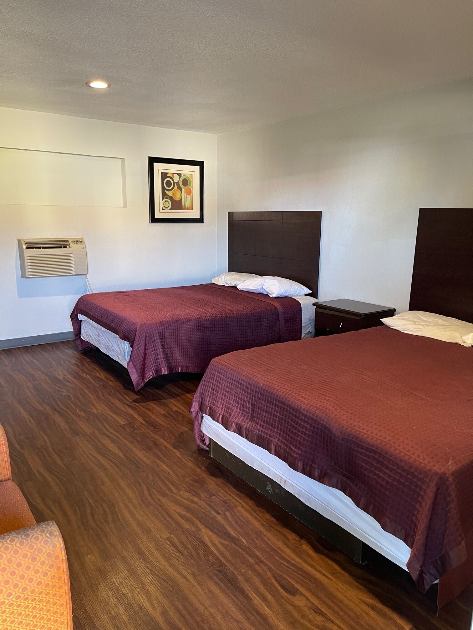 A hotel room with two beds, a nightstand, a wall-mounted air conditioner, and a framed picture.