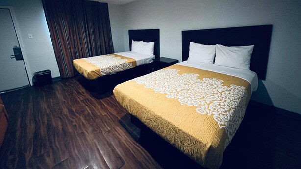 A hotel room with two beds, wooden flooring, a dark headboard, and a curtain. - Richmond Motel (Richmond)