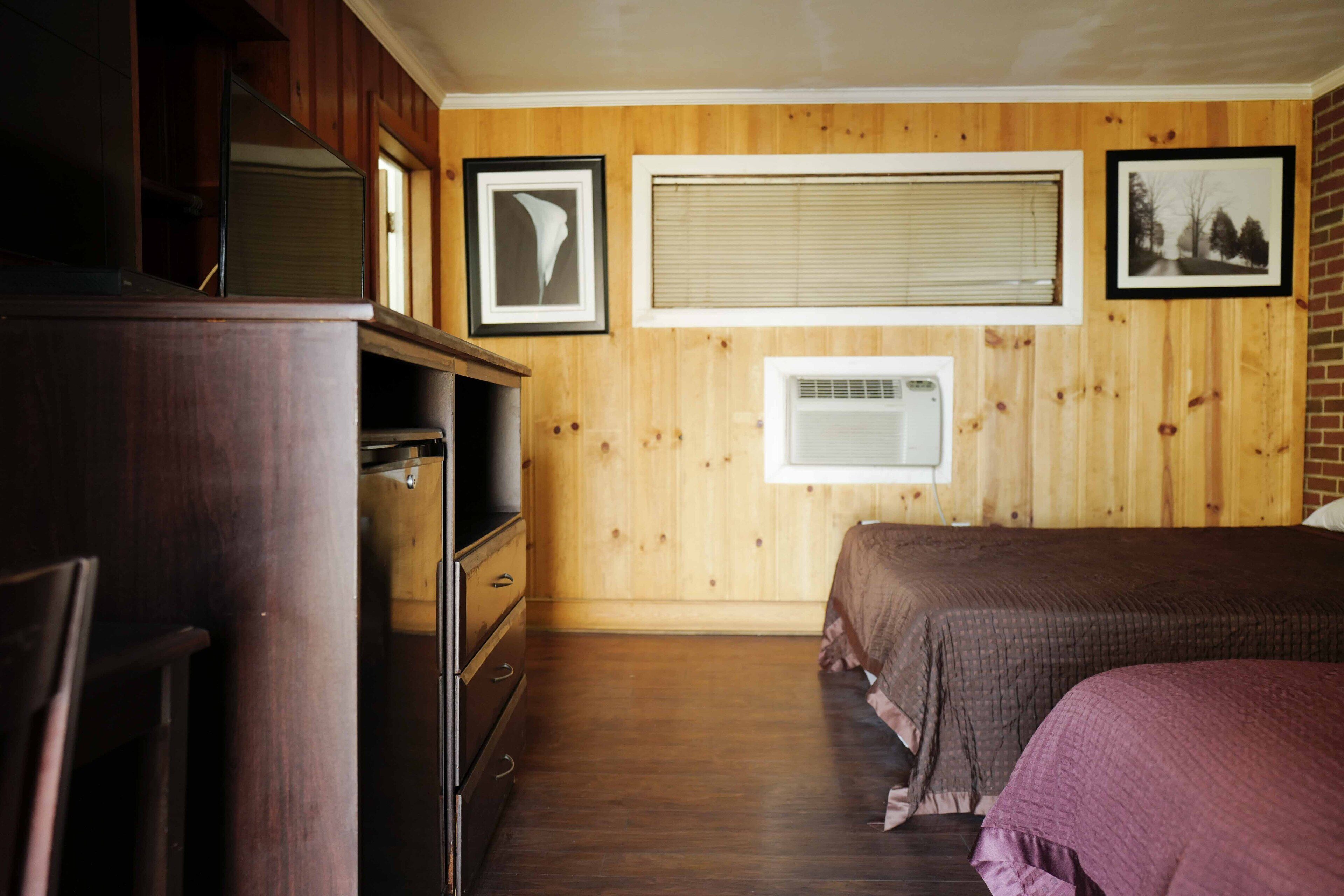A bedroom with wooden walls, a bed, a dresser, and a window with blinds.