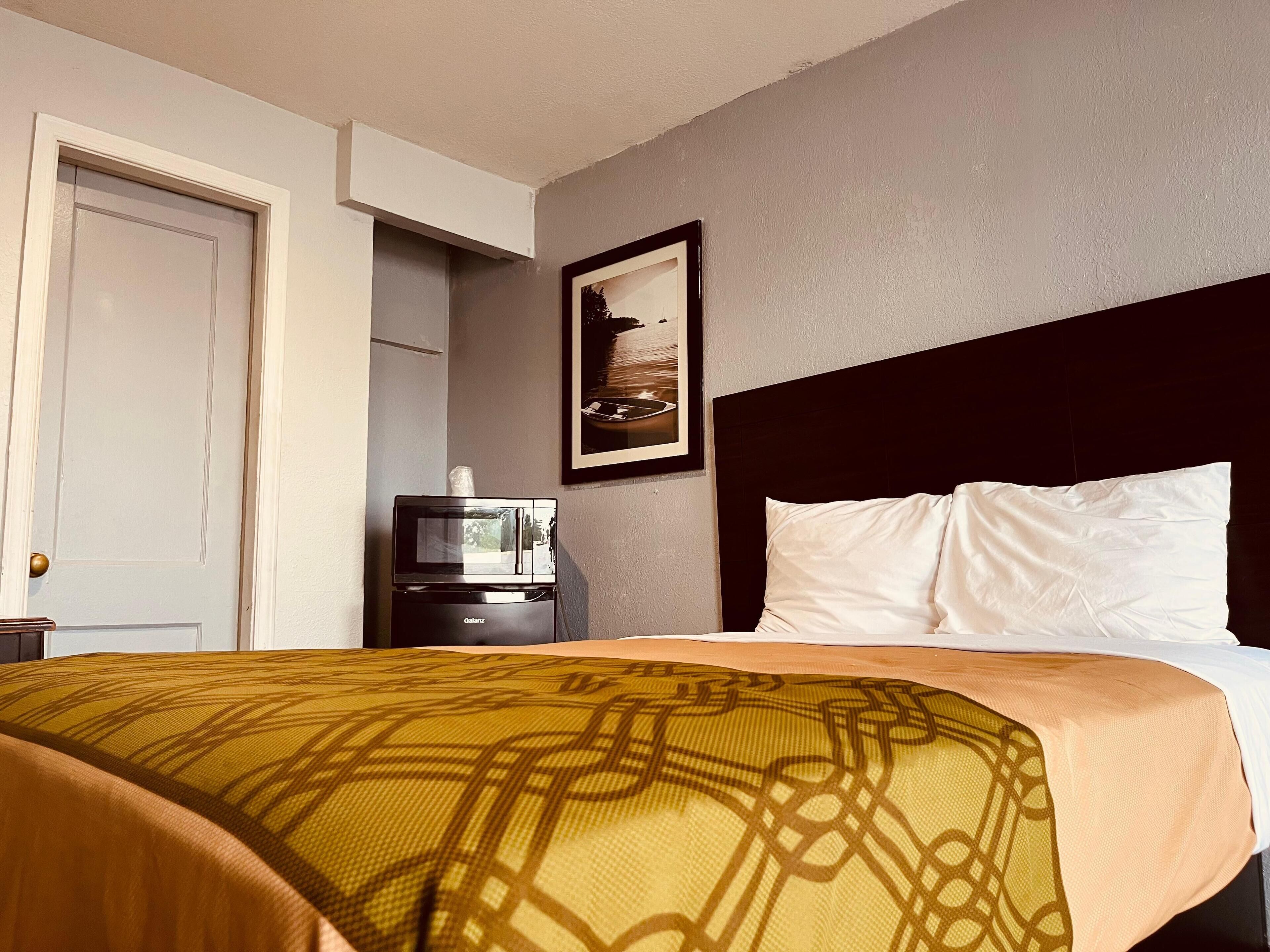 A hotel room with a bed, a television on a stand, and a framed picture on the wall.