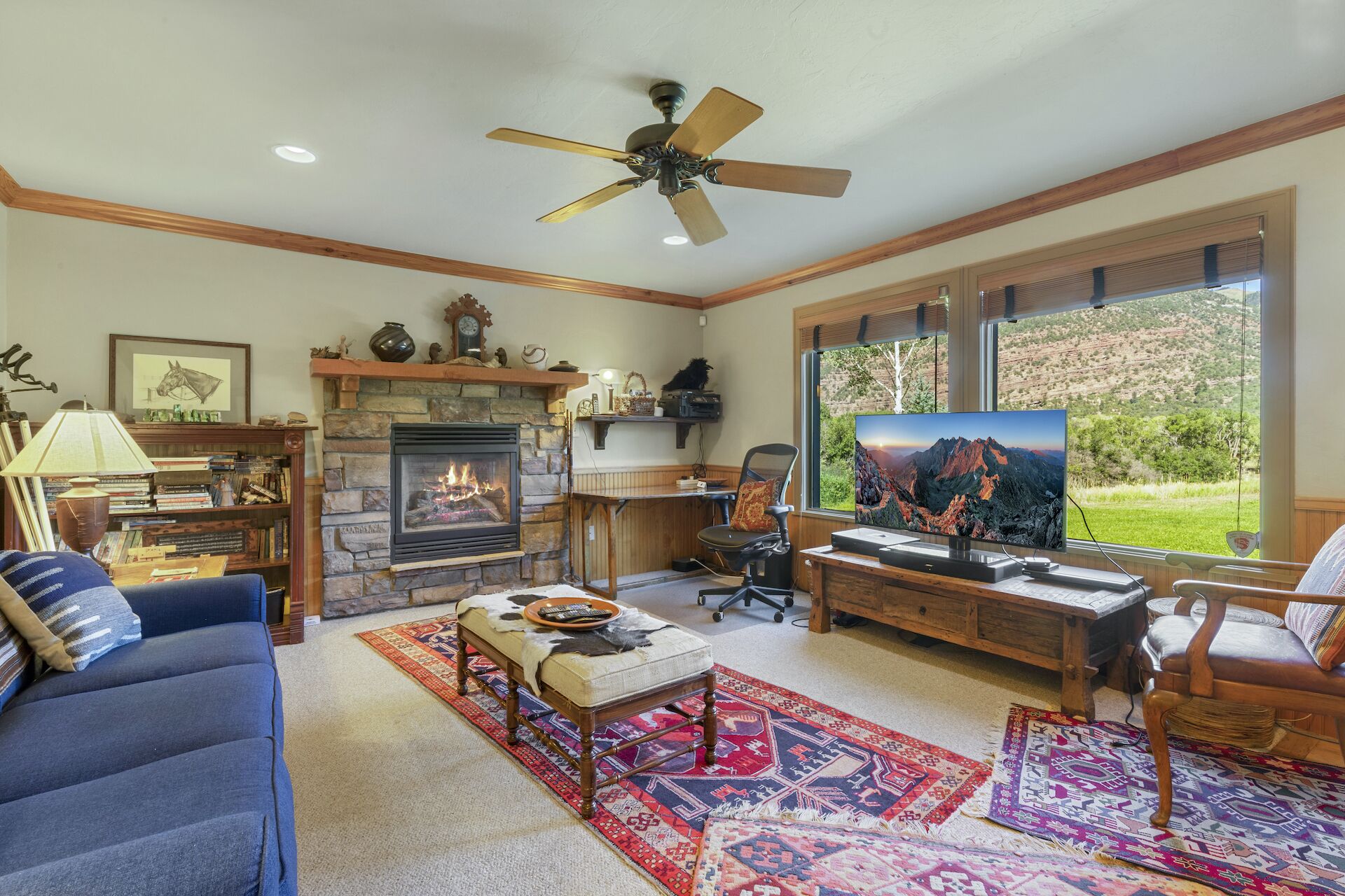 Una sala de estar con chimenea de piedra, televisor, escritorio y un ventanal con vistas al exterior.