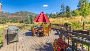 Une terrasse en bois avec une table et des chaises sous un parasol rouge, un barbecue et un jardinière.