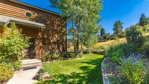 Une maison en bois avec des fondations en pierre, une pelouse bien entretenue et une variété de plantes et de fleurs.