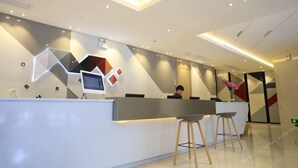 A modern reception area with a geometric wall design, a reception desk, and two bar stools. - Borrman Hotel (Guangzhou Tianhe Sports Center Linhe West Metro Station) (Guangzhou)