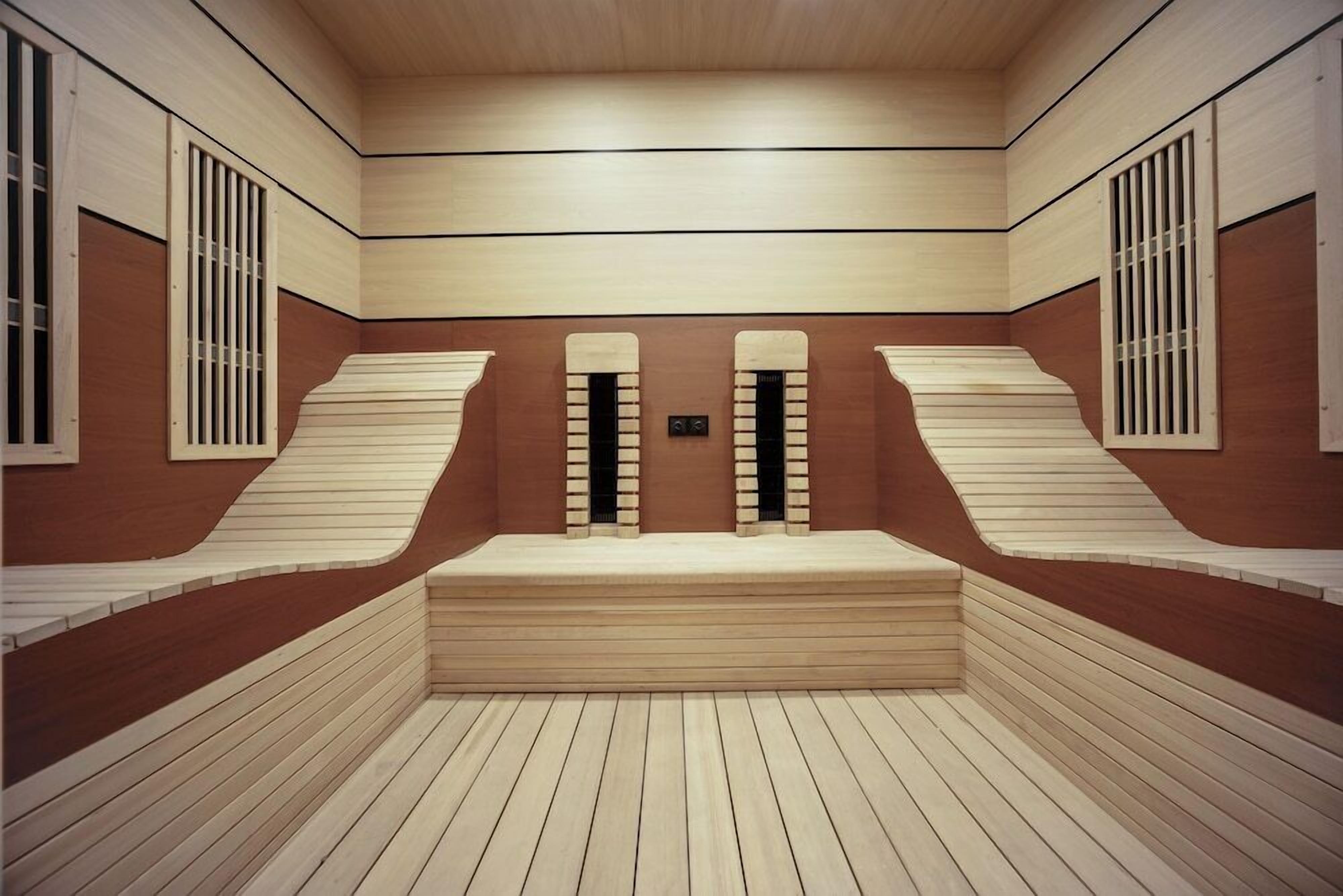 A room with a wooden floor, a central bench, and two windows with vertical bars.