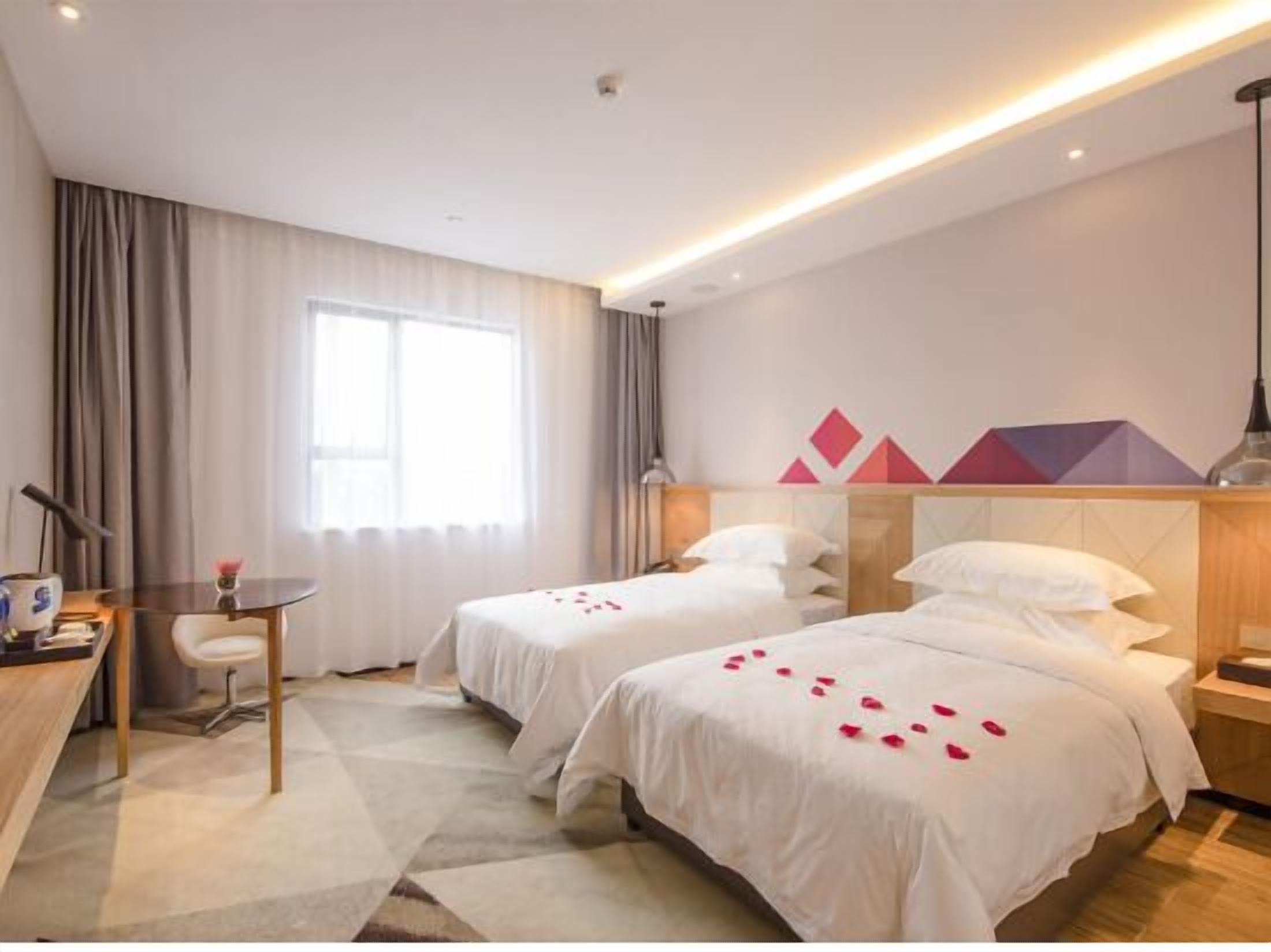 A hotel room with two beds, a desk, a chair, and a window with curtains.