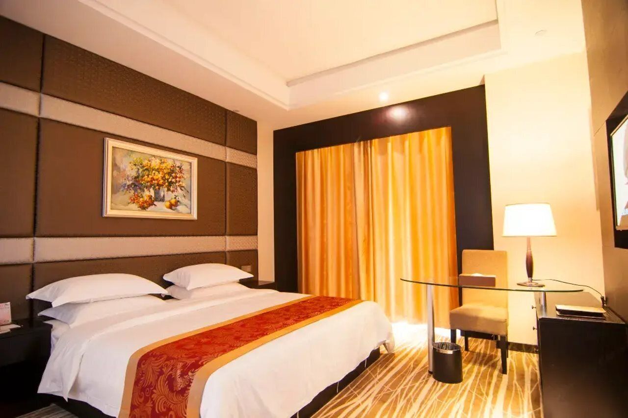 Habitación de hotel con una cama grande, un escritorio con lámpara, una silla y un cuadro en la pared.