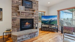 Un salon moderne doté d’une cheminée en pierre, d’un téléviseur à écran plat et offrant une vue sur les montagnes grâce à de grandes fenêtres.