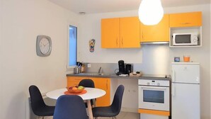 Een kleine keuken met oranje kastjes, een magnetron, een koelkast, een koffiezetapparaat en een klok aan de muur.