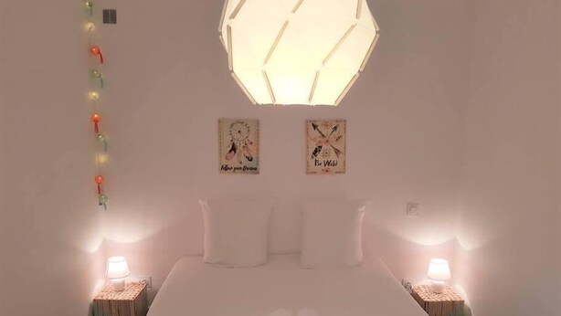Een slaapkamer met een groot bed, twee nachtkastjes met lampen, een geometrisch plafondlamp en twee kunstwerken aan de muur.