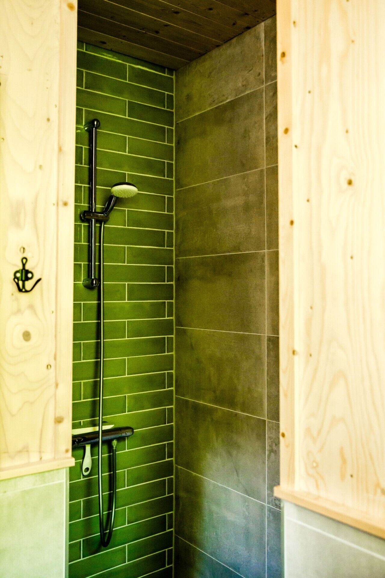 Een douche met een wand betegeld met groene tegels en een houten deur.