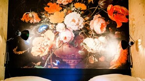 Una cama con una gran obra de arte floral sobre ella, dos lámparas a cada lado y un cabecero de madera.