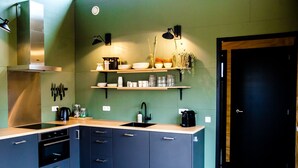 A modern kitchen with a stainless steel range hood, built-in oven, and a double sink. There are wooden shelves above the sink holding dishes and glasses. - Nature lodge Ljurk, Akkrum - sleeps 4, dogs welcome (Akkrum)