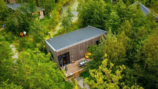 A modern building surrounded by dense forest, with a wooden deck and outdoor seating area.