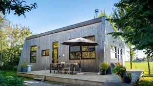 Eine moderne Holzhütte mit einer Terrasse, Sitzgelegenheiten im Freien und Blumentöpfen.