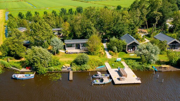 A lakeside property with docked boats, a wooden pier, and a house surrounded by lush greenery. - Nature lodge Reade Wikel, Akkrum - children`s sleeping hut (Akkrum)