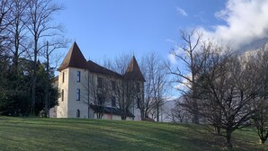 A large, historic building with a prominent tower and multiple windows, surrounded by a grassy area and leafless trees.