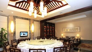 A dining area with a round table set for a meal, surrounded by chairs, with a television on the wall and a decorative wall panel in the background. - Haiyan International Hotel (Jiaxing)
