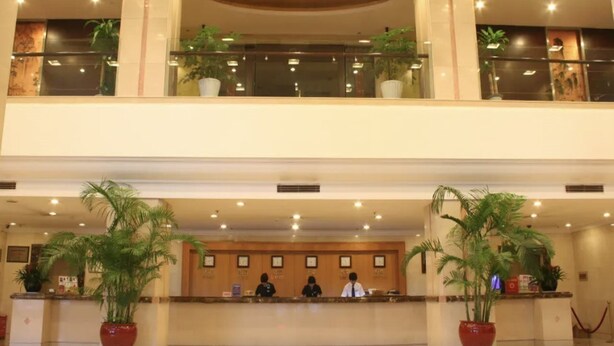 A hotel lobby with a reception desk, two floors, and potted plants. - Haiyan International Hotel (Jiaxing)