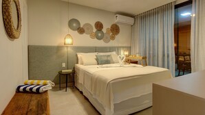 A modern bedroom with a large bed, a bedside table, a wall-mounted air conditioner, and a view of the outside through a window with curtains. - Apto térreo com TV 4k no Wai Wai Cumbuco (Caucaia)