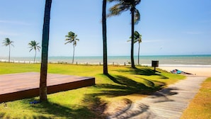 A wooden deck leading to a beach with palm trees and a clear view of the ocean. - Apto térreo com TV 4k no Wai Wai Cumbuco (Caucaia)