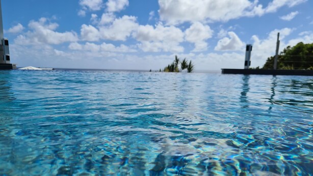 Ein klares Schwimmbecken mit sichtbaren Wellen und einem entfernten Blick auf ein Gebäude und Bäume.
