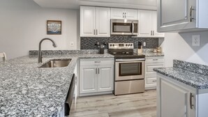 Eine moderne Küche mit weißen Schränken, Granit Arbeitsplatten, Edelstahlgeräten und einer schwarzen Spritzschutzwand.