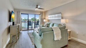 Ein modernes Wohnzimmer mit einer Couch, einem Fernseher, einem Deckenventilator und Blick ins Freie.