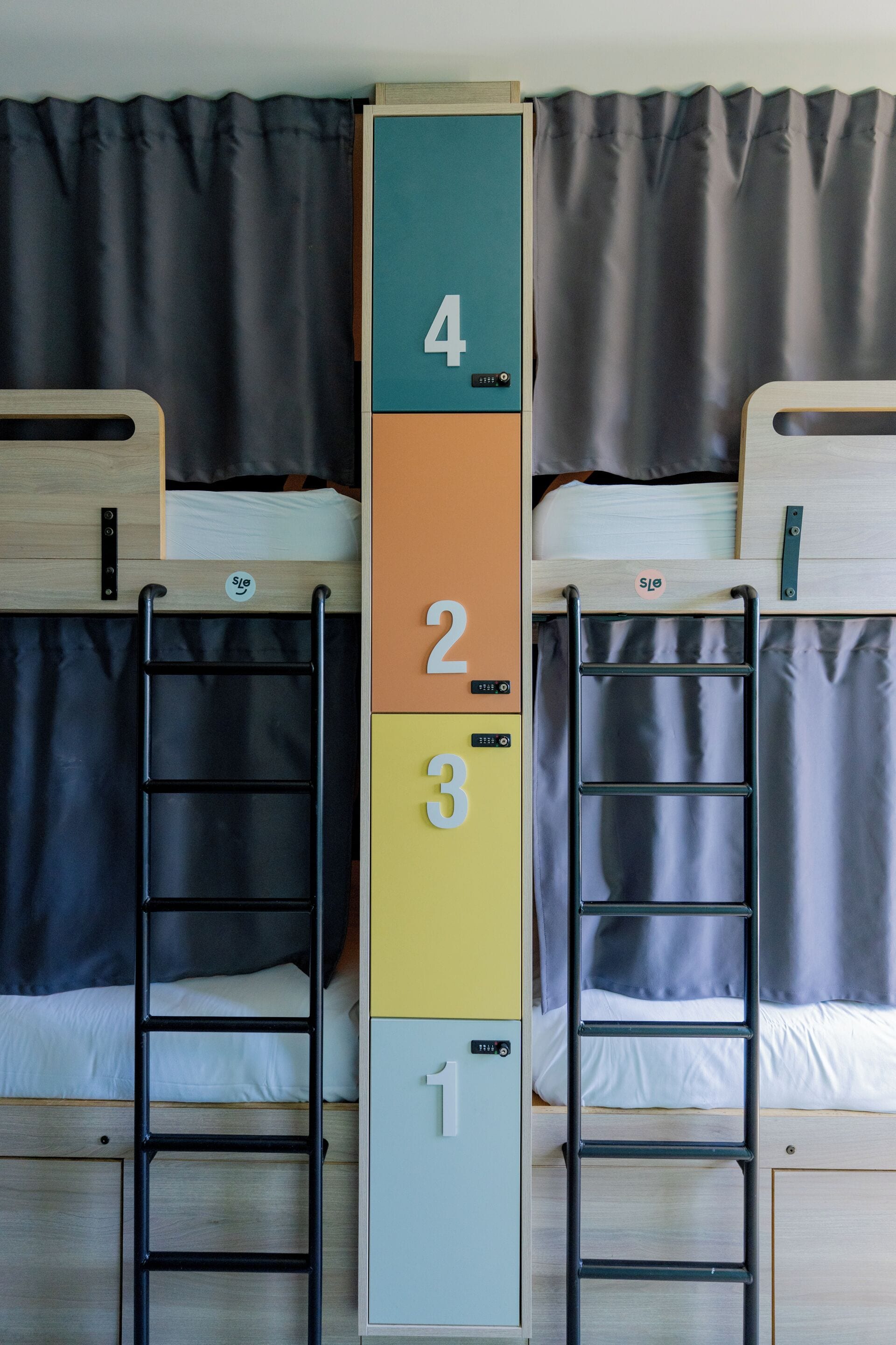 Tweepersoonsbedden met bevestigde ladders, genummerde opbergvakken en een gordijnen achtergrond.