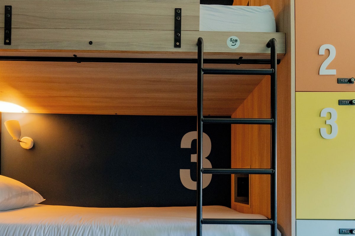 Un lit superposé avec une échelle, une table de chevet et une armoire avec des compartiments numérotés.